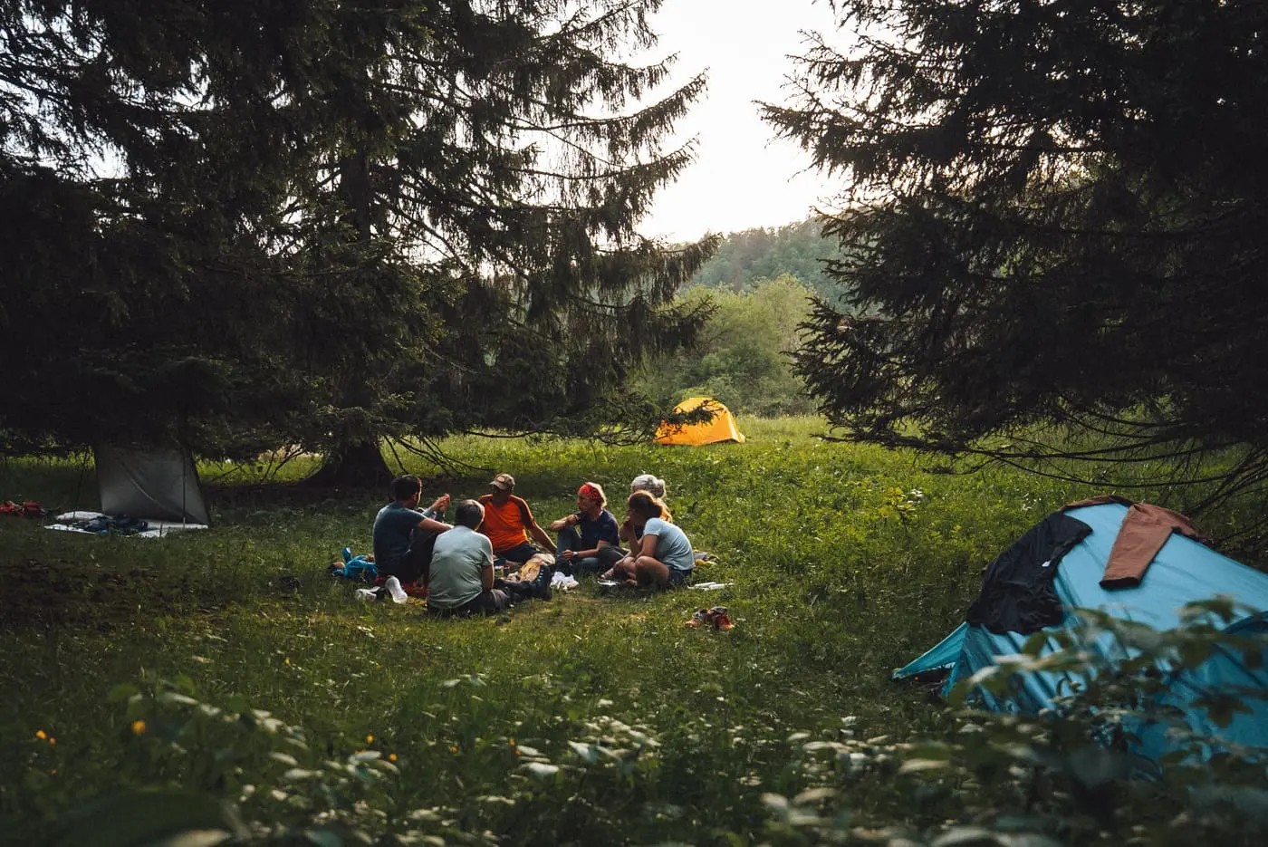 Petit groupe en bivouac autour de tentes dans une clairière au coucher du soleil